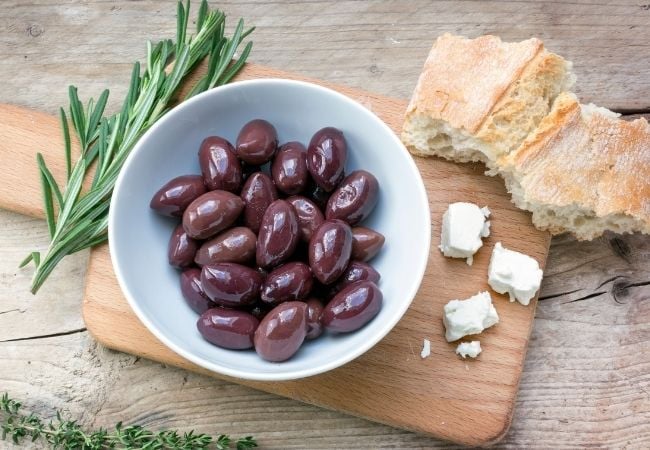 Bowl of Kalamata olives on cutting board with bread and fresh rosemary