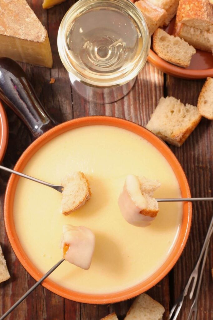 Photo of Easy Cheese Fondue Recipe with Fondue Forks with Bread Cubes and a Glass of Wine 