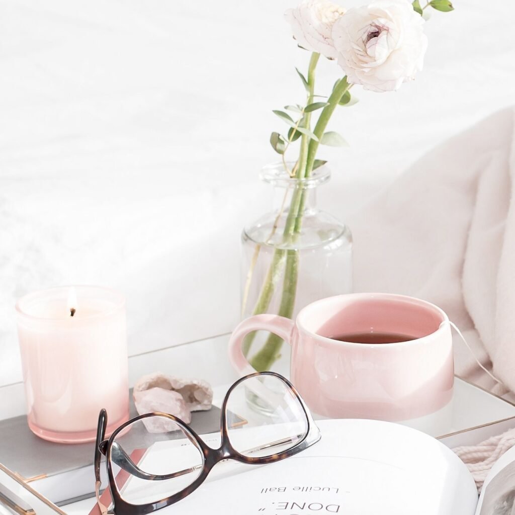 55 Simple Pleasures in Life - Bed side table with coffee mug, vase with rose, candle, and glasses.