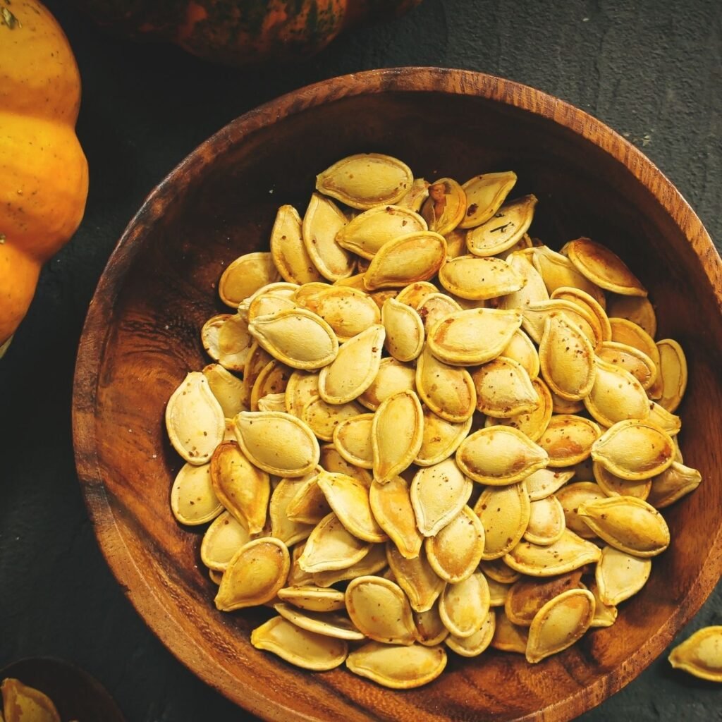 How to Roast Pumpkin Seeds - Roasted Pumpkin seeds in a wooden bowl next to a pumpkin