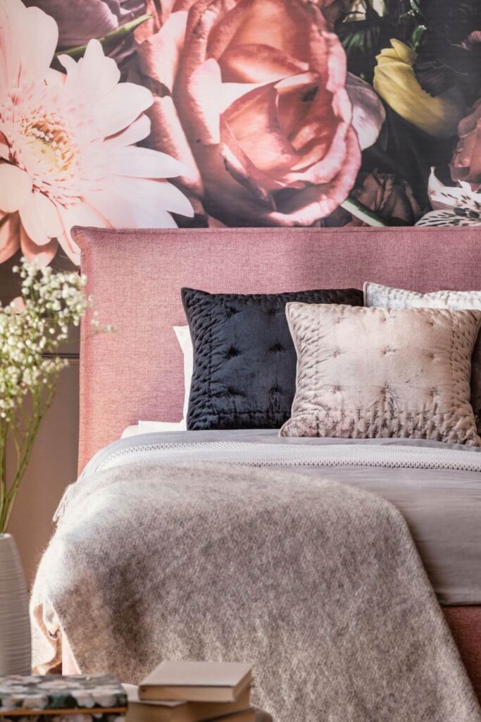 The Best Hygge Bedrooms - Pink Fabric Headboard -his charming bedroom features a soft pink fabric headboard that adds a touch of romance against a backdrop of vintage-inspired floral wallpaper. Gray and black accents throughout the space—like crisp gray bedding and sleek lighting—create a stylish contrast that feels both fresh and timeless. Perfect for lovers of feminine bedroom ideas, floral wallpaper trends, and cozy yet elegant spaces, this look blends classic beauty with modern flair.
