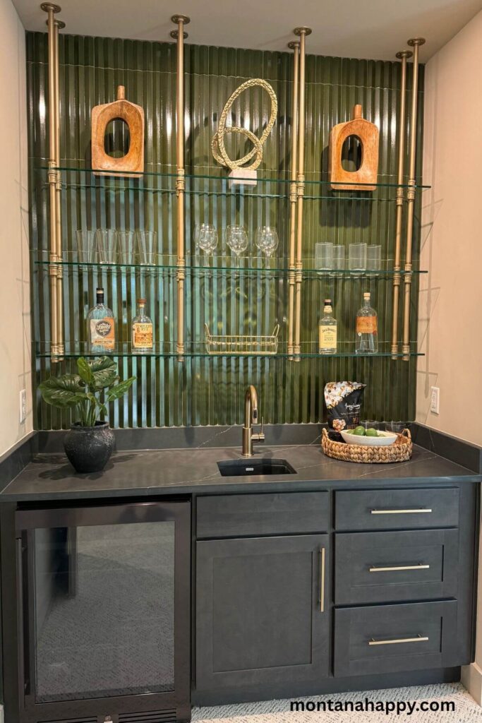 Modern Home Decor Ideas - Modern Built-In Wet Bar Design - A dark green glass-tile backsplash glows softly behind brass poles that support sleek glass shelves, giving this wet bar a refined, modern edge. The dark cabinetry, paired with a built-in mini fridge, creates a sophisticated little corner perfect for mixing drinks in style.