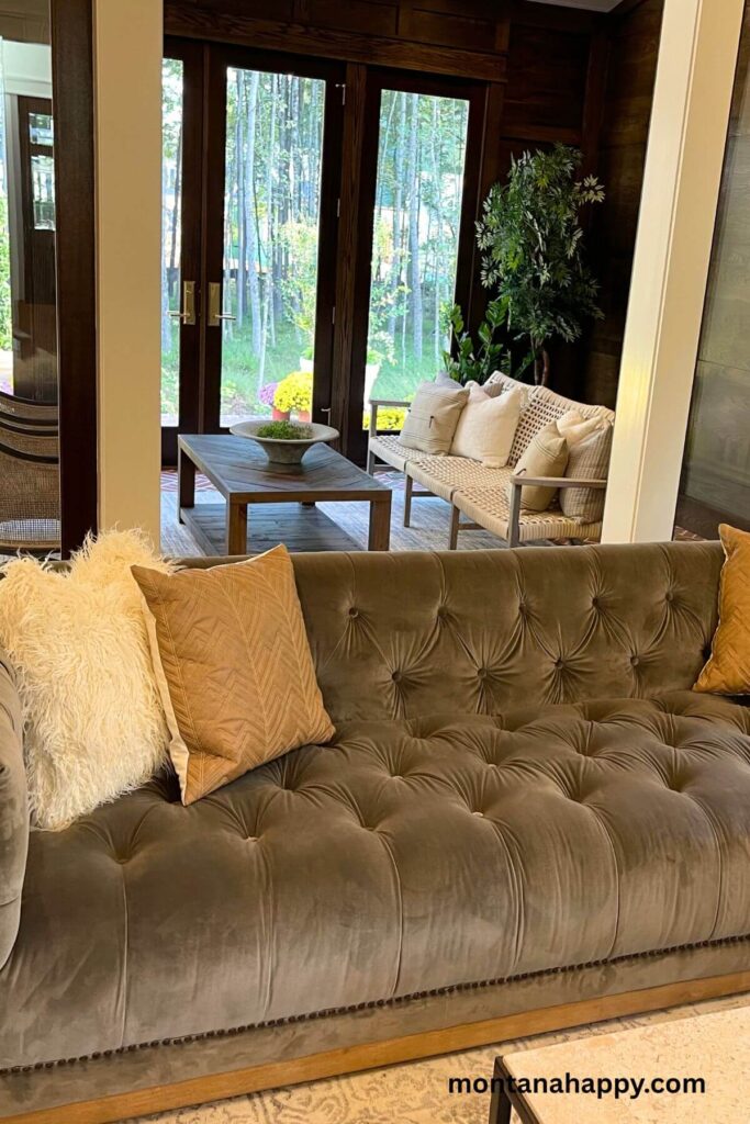 Modern Living Room Inspiration -A cozy living room features a soft gray tufted couch that invites you to sink in and unwind, perfectly positioned behind an enclosed porch that fills the space with gentle natural light.