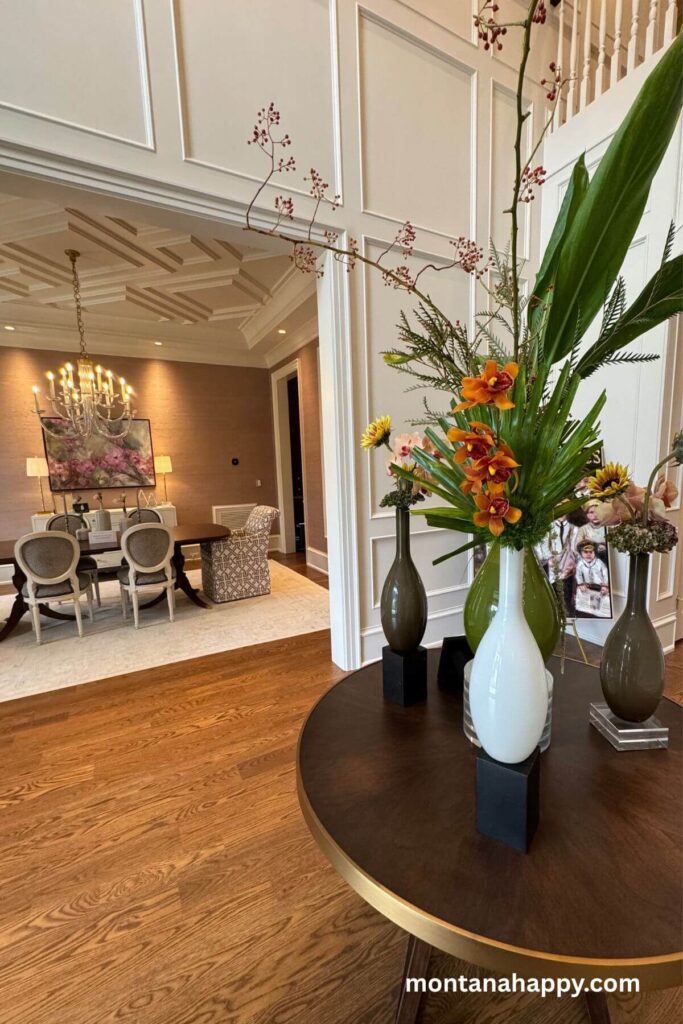 Modern Home Decor Ideas - Photo of Modern Entry Way Design and Elegant Dining Room -The grand entryway sets an elegant tone with its round wooden table topped with lush florals, creating a warm and sophisticated welcome. Just beyond, a peek into the formal dining room with its soft lighting hints at the luxurious spaces that flow throughout the home.