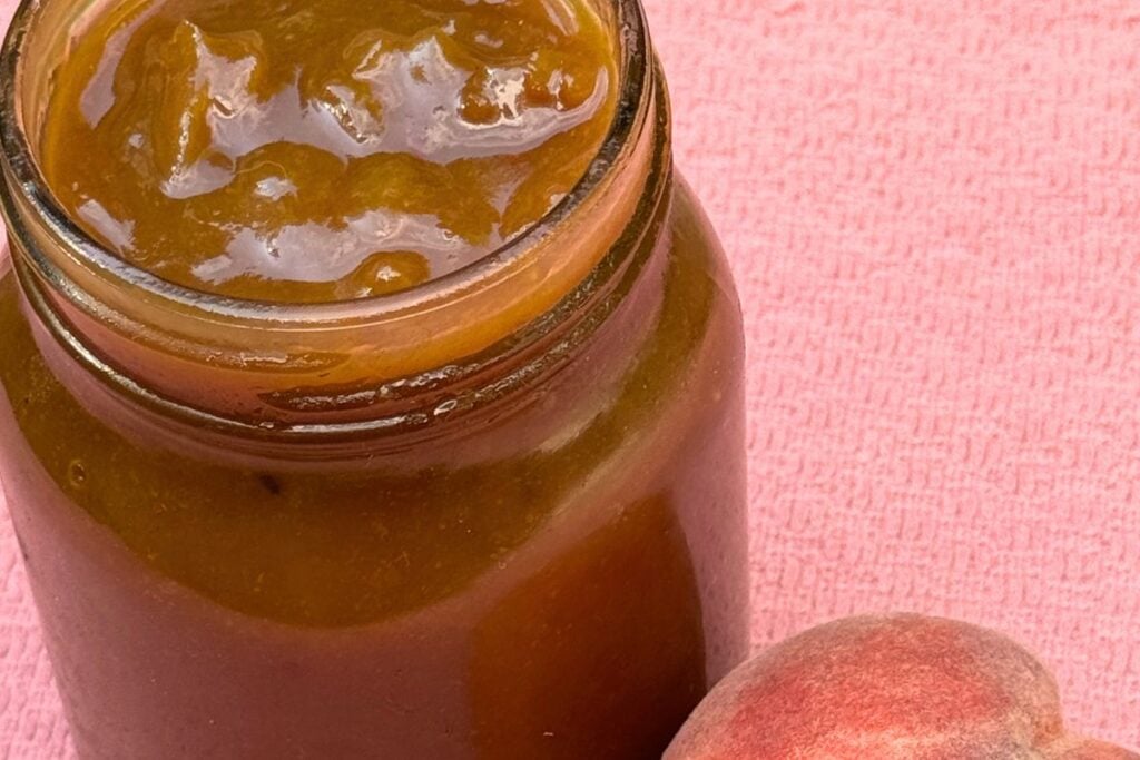Photo of Peach Bourbon BBQ Sauce Recipe in a Mason Jar with a Fresh Peach 