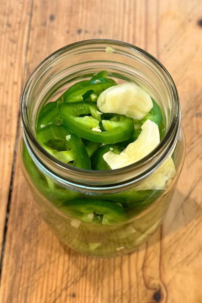 Quick Pickled JalapeƱos Recipe - Photo of JalapeƱo Slices and Smashed Garlic in Mason Jar